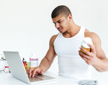 Athlete Using Laptop While Holding Sports Nutrition Supplement