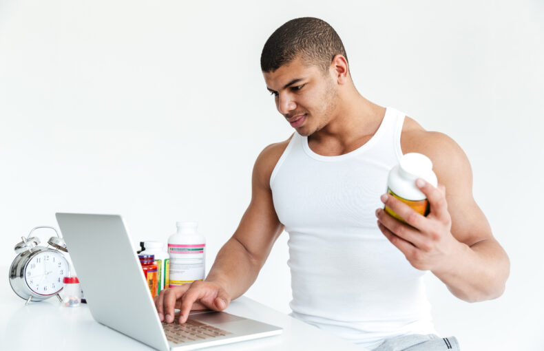 Athlete Using Laptop While Holding Sports Nutrition Supplement